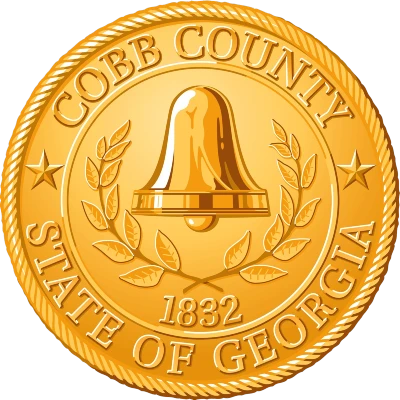 Cobb COunty Logo with in a gold coin style with bell in the middle and some leaves. Some text and 1832 written on it
